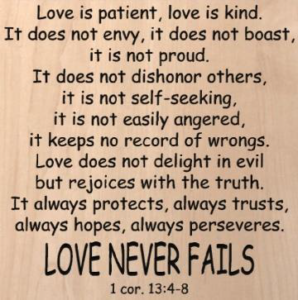 wood sign that says "Love is patient, love is kind. It does not envy, it does not boast, it is not proud. It does not dishonor others, it is not self-seeking, it is not easily angered, it keeps no record of wrongs. Love does not delight in evil but rejoices with the truth. It always protects, always trusts, always hopes, always perseveres. Love never fails. 1 Corinthians 13:4-8"
