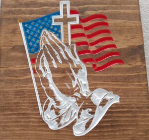 wood sign with prayer hands and an american flag and cross slightly behind the hands