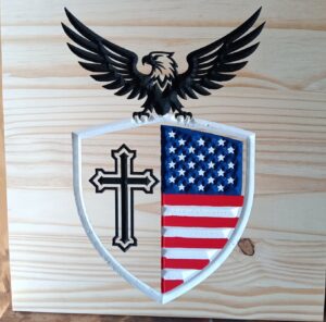 wood sign with a bald eagle holding up a shield with a cross on half of it and an american flag on the other half