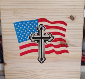 wood sign with american flag waving in the background and a cross in the foreground