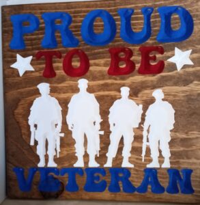 wood sign with four veterans standing in a line, also has text that says "Proud to be Veteran"
