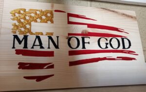 wood sign with a red and gold american flag with a cross on top of it and "man of God" written across the middle in black