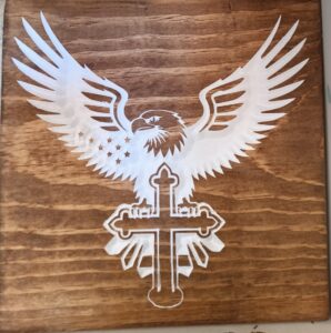 wood sign with a white bald eagle sitting on a cross with it's wings spread upward.