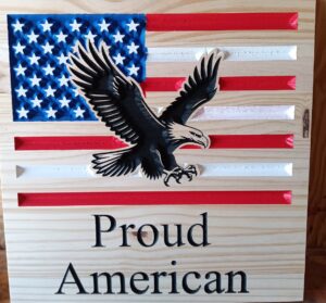 wood sign wiyh "Proud American" written on the bottom and an american flag with an eagle with talons outstretched above the text