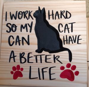 Wood sign with cat and paw prints, text on sign says "I work hard so my cat can have a better life"