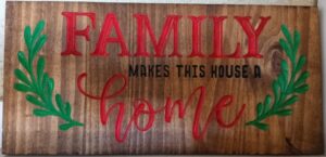 wood sign with green vines and red/black text saying: "Family makes this house a home"
