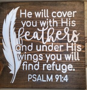 wood sign with a white feather on the left and text that says "He will cover you with His feathers and under His wings you will find refuge. Psalm 91:4"
