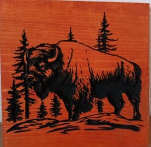 wood sign with realistic bison standing in front of pine trees, wood is a red color