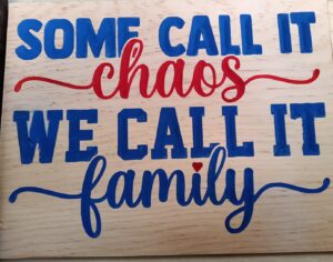 wood sign with blue and red text saying: " Some call it chaos, we call it family"