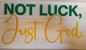 wood sign with green and yellow letters that says "Not luck, just God."