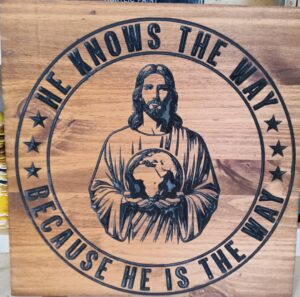 Wood sign with Jesus in the middle holding the world in his hands. A circle surrounding him with the text "He knows the way because he is the way" in it