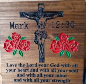 wood sign with Jesus on the cross and "Mark 12:30" on the sides of it. Two rose clusters on either side underneath the cross. "Love the Lord your God with all your heart and with all your soul and with all your mind and with all your strength"